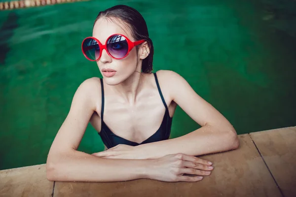 Belle femme brune en lunettes de soleil drôles avec un maquillage professionnel flottant dans la piscine . — Photo