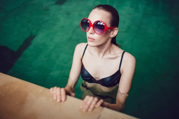 Hermosa mujer morena en gafas de sol divertidas con un maquillaje profesional flotando en la piscina . — Foto de Stock