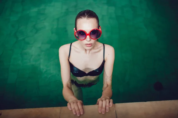 Hermosa mujer morena en gafas de sol divertidas con un maquillaje profesional flotando en la piscina . — Foto de Stock