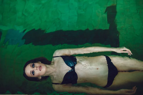 Mulher morena sexy com uma bela maquiagem profissional flutuando na piscina . — Fotografia de Stock