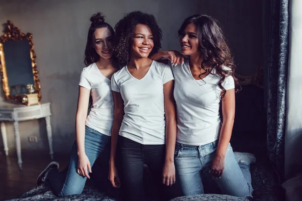 Hermosas chicas sonrientes divirtiéndose en camisas blancas en la cama. Camiseta maqueta . — Foto de Stock