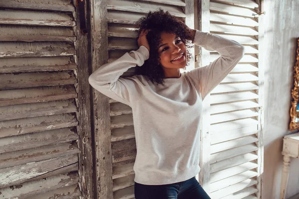 Hermosa chica africana vestida con sudadera en blanco de pie sobre fondo de pared de madera. Mock-up . —  Fotos de Stock