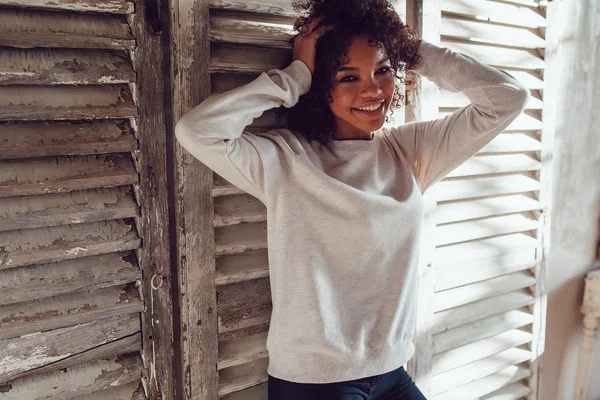 Hermosa chica africana vestida con sudadera en blanco de pie sobre fondo de pared de madera. Mock-up . —  Fotos de Stock