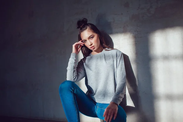 Mooi meisje gekleed in lege sweatshirt zittend op een grijze achtergrond. Mock-up. — Stockfoto