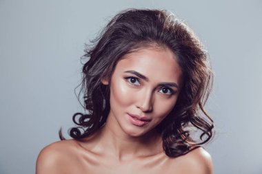 Esmer kız parlak dalgalı saçlı ve güzel yapmak gri arka plan üzerinde stüdyoda poz.