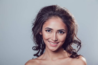 Esmer kız parlak dalgalı saçlı ve güzel yapmak gri arka plan üzerinde stüdyoda poz.