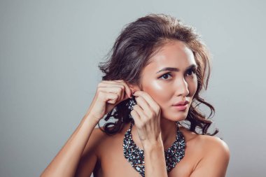 Kalıcı makyaj ve stil genç kadınla güzel küpe üzerinde çalışır. Gri arka planı.