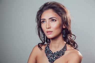 Makyaj şık kolye ve küpe gri bir arka plan üzerinde olan güzel kadın.