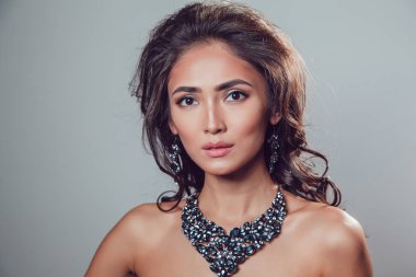 Makyaj şık kolye ve küpe gri bir arka plan üzerinde olan güzel kadın.