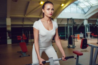 Güzel kız simülatör spor egzersizleri yapıyor boş beyaz t-shirt ve tayt giymiş. Yukarı alay.