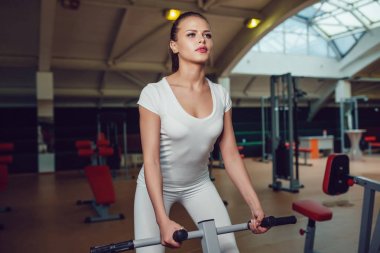 Güzel kız simülatör spor egzersizleri yapıyor boş beyaz t-shirt ve tayt giymiş. Yukarı alay.