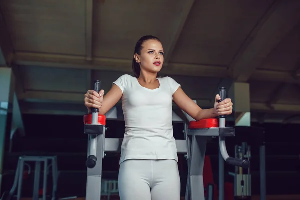 Hermosa chica haciendo ejercicios en el simulador en el gimnasio vestido en blanco camiseta blanca y medias. Prepárate. . —  Fotos de Stock