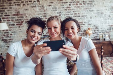 Güzel kızlar eğleniyor ve yatağın oturan selfie yapmak.