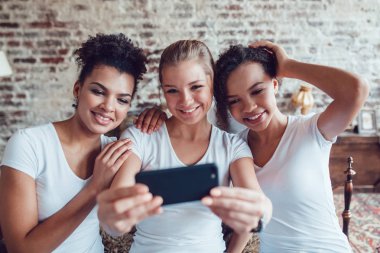 Güzel kızlar eğleniyor ve yatağın oturan selfie yapmak.