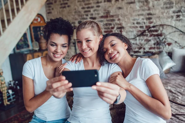 Ładne dziewczyny zabawy i zrobić selfie siedzi koło łóżka. — Zdjęcie stockowe