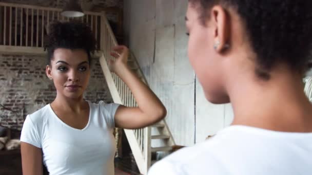 Menina afro-americana atraente corrige o cabelo em pé na frente de um espelho . — Vídeo de Stock