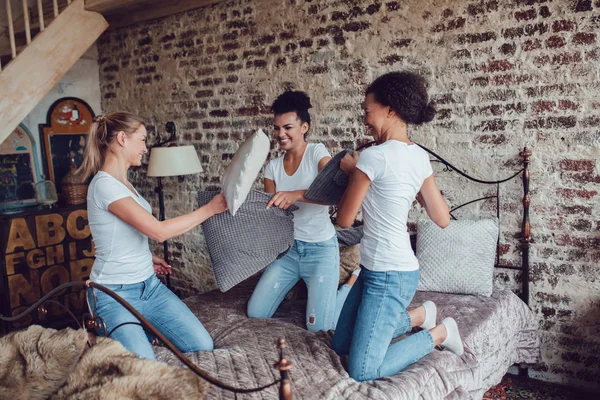Chicas atractivas se divierten y luchan almohadas en la cama . — Foto de Stock