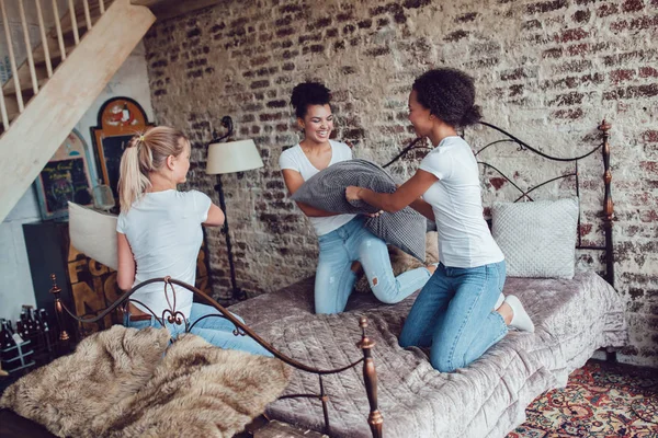 Chicas atractivas se divierten y luchan almohadas en la cama . — Foto de Stock