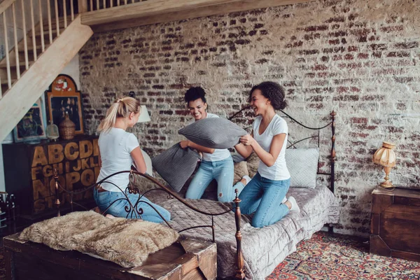 Chicas atractivas se divierten y luchan almohadas en la cama . — Foto de Stock