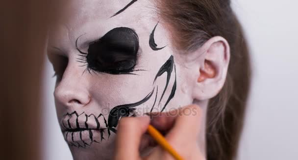 Maskenbildnerin schminkt das Mädchen zu Halloween auf weißem Hintergrund. Halloween-Gesichtskunst. — Stockvideo