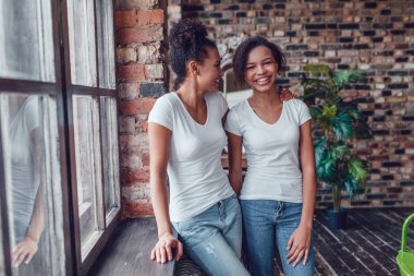 Beyaz T-shirt'de iki çekici Afro-Amerikan kız pencerenin duruyorsun.