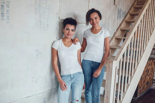 Duas meninas americanas africanas atraentes em camisetas brancas estão de pé perto das escadas . — Fotografia de Stock