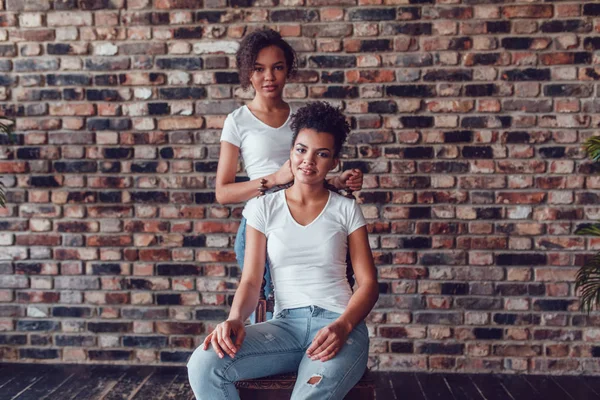Dos chicas afroamericanas atractivas en camisetas blancas sobre un fondo de pared de ladrillo . — Foto de Stock