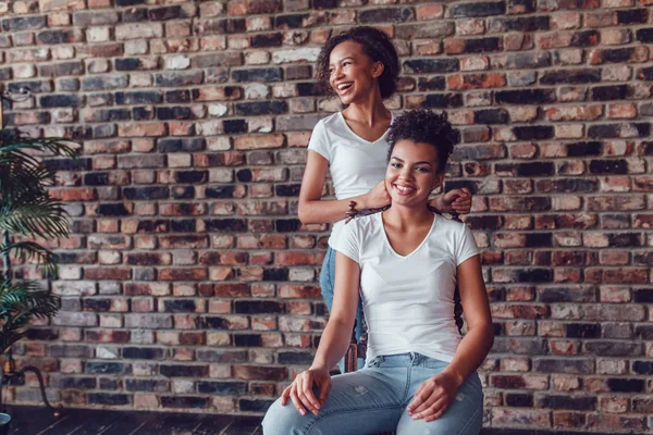 Dos chicas afroamericanas atractivas en camisetas blancas sobre un fondo de pared de ladrillo . —  Fotos de Stock