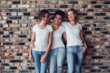 Beyaz T-shirt üç çekici kız bir tuğla duvar arka plan üzerinde duruyorsun.