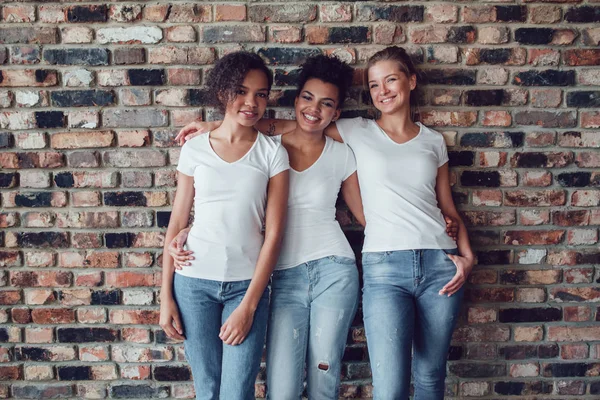Trzy atrakcyjne dziewczyny w białych koszulkach stoją na tle ściany Cegła. — Zdjęcie stockowe