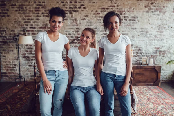 Trzy atrakcyjne dziewczyny w białych koszulkach siedzą w domu koło łóżka. — Zdjęcie stockowe
