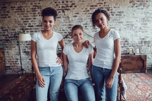 Tres chicas atractivas en camisetas blancas están sentadas en casa cerca de la cama . — Foto de Stock