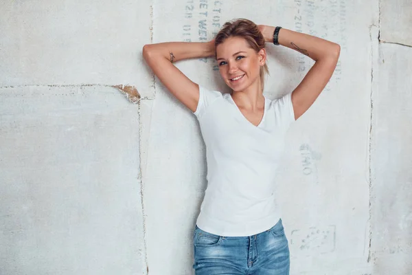 Atractiva mujer rubia con una camiseta blanca se levanta sobre un fondo claro . — Foto de Stock