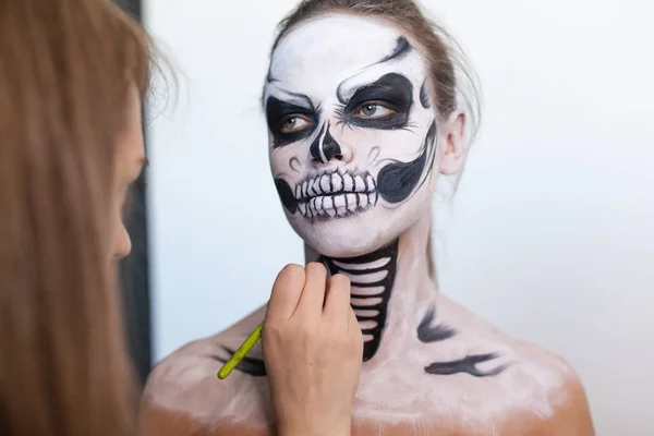 Maskenbildnerin schminkt das Mädchen zu Halloween auf weißem Hintergrund. Halloween-Gesichtskunst. — Stockfoto