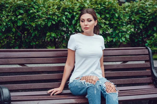 Attractive girl in white sits on a bench in the park. — Stock Photo, Image