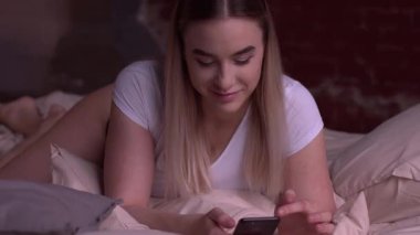 Seksi sarışın kadın yatakta yatıyordu ve smartphone kullanarak.