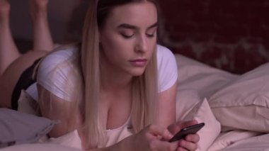 Seksi sarışın kadın yatakta yatıyordu ve smartphone kullanarak.