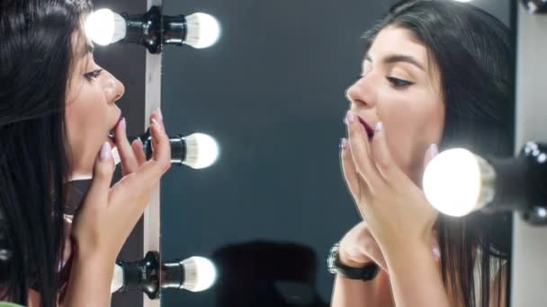 Красивая женщина красит губы, глядя в зеркало. Делать макияж губ . — стоковое видео