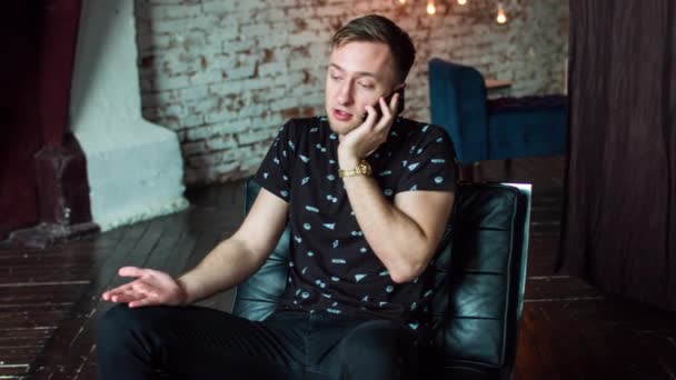 Homem atraente falando ao telefone sentado na poltrona . — Vídeo de Stock