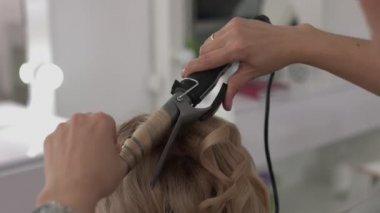 Saç stilisti bir kıvırcık saç şekillendirme kullanan bir kız için yapar. Kuaför iş başında.