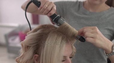 Saç stilisti bir kıvırcık saç şekillendirme kullanan bir kız için yapar. Kuaför iş başında.