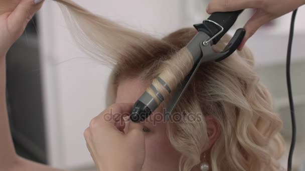 Στυλίστας μαλλιά κάνει μια μπούκλες για ένα κορίτσι, χρησιμοποιώντας styling μαλλιών. Κομμωτήριο στο χώρο εργασίας. — Αρχείο Βίντεο
