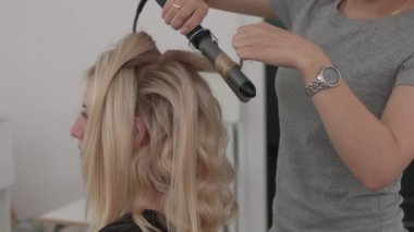 Saç stilisti bir kıvırcık saç şekillendirme kullanan bir kız için yapar. Kuaför iş başında.