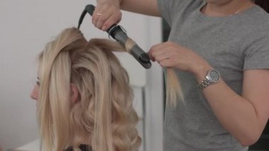 Saç stilisti bir kıvırcık saç şekillendirme kullanan bir kız için yapar. Kuaför iş başında.