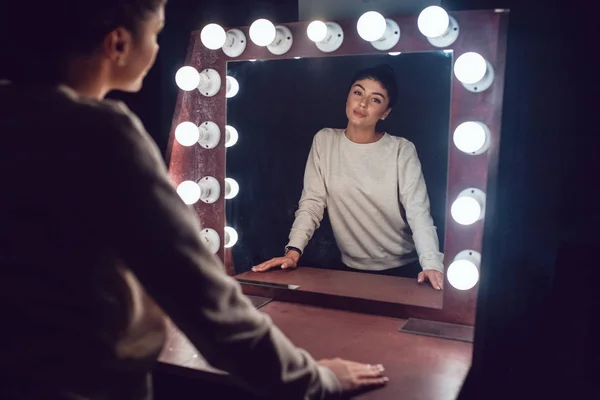 Приваблива брюнетка в сірому светрі дивиться у дзеркало . — стокове фото