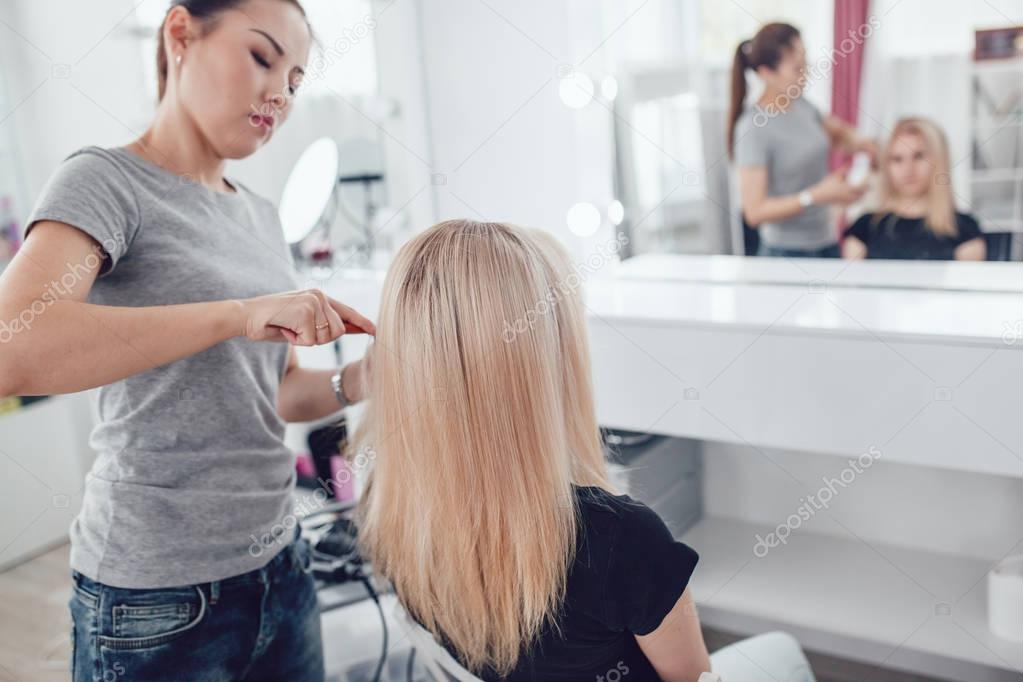 Hair-stylist by hair combs girl hair in beauty studio.