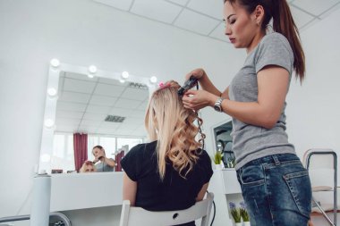 Saç stilisti bir kıvırcık saç şekillendirme kullanan bir kız için yapar. Kuaför iş başında.