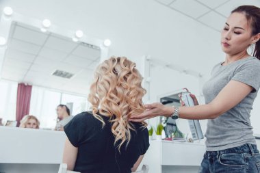 Saç stilisti bir kıvırcık saç şekillendirme kullanan bir kız için yapar. Kuaför iş başında.