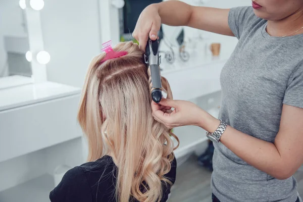 Стиліст волосся робить завитки для дівчини, використовуючи зачіску. Перукар на роботі . — стокове фото