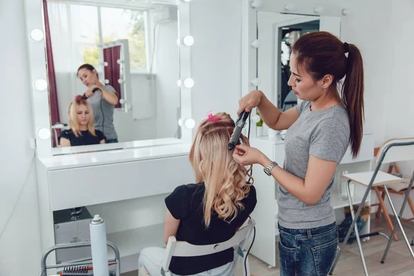 Peluquero hace un rizos para una chica, usando peinado. Peluquería en el trabajo . — Foto de Stock